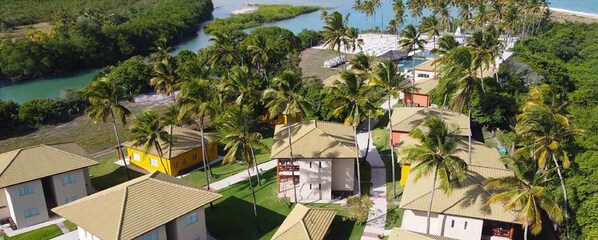 Área residencial à beira-mar, com casas, palmeiras e uma praia.