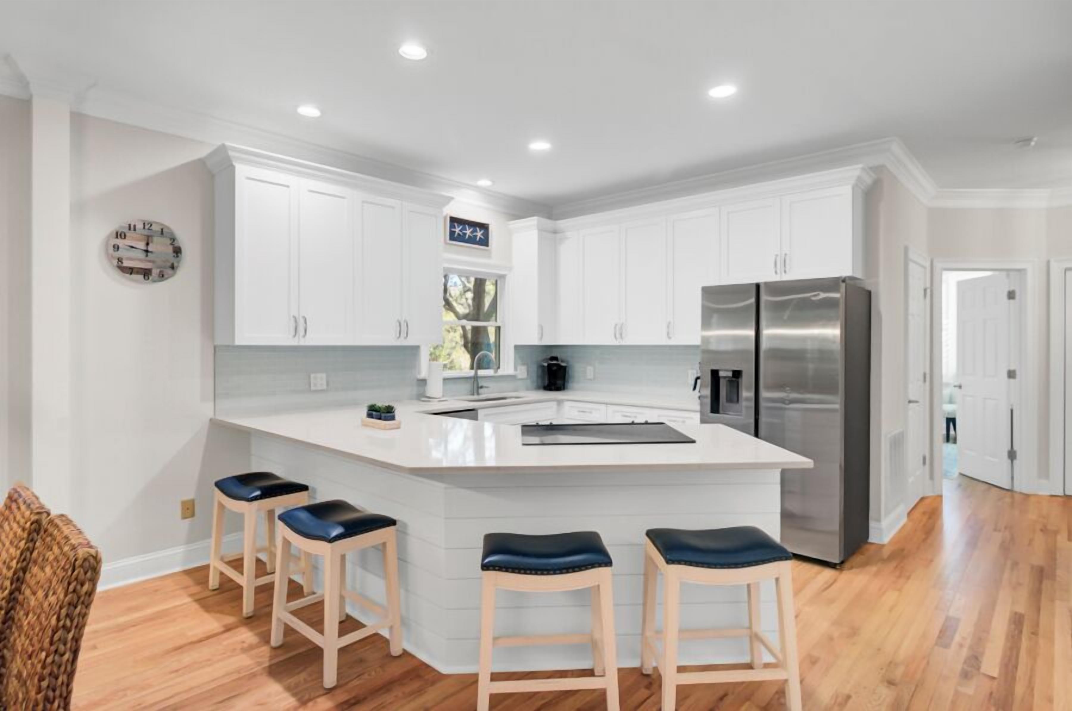 Una cocina moderna con armarios blancos, un refrigerador de acero inoxidable y una isla central con taburetes de bar.