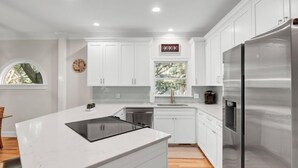 A modern kitchen with white cabinetry, a stainless steel refrigerator, and a window with a view of trees. - Award-Winning Resort Amenities | Grand Pavilion 09 (Isle of Palms)