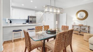 A modern kitchen with white cabinets, a stainless steel refrigerator, and a glass dining table with wicker chairs. - Award-Winning Resort Amenities | Grand Pavilion 09 (Isle of Palms)