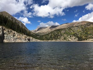 A mountain landscape with a clear lake, rocky terrain, and dense forests.