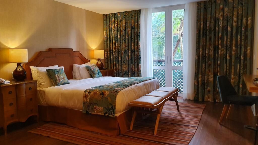 A hotel room with a large bed, a bench, a desk, and a chair.