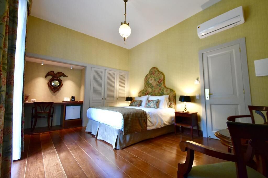 Quarto com cama, mesas de cabeceira, escrivaninha e uma cadeira.