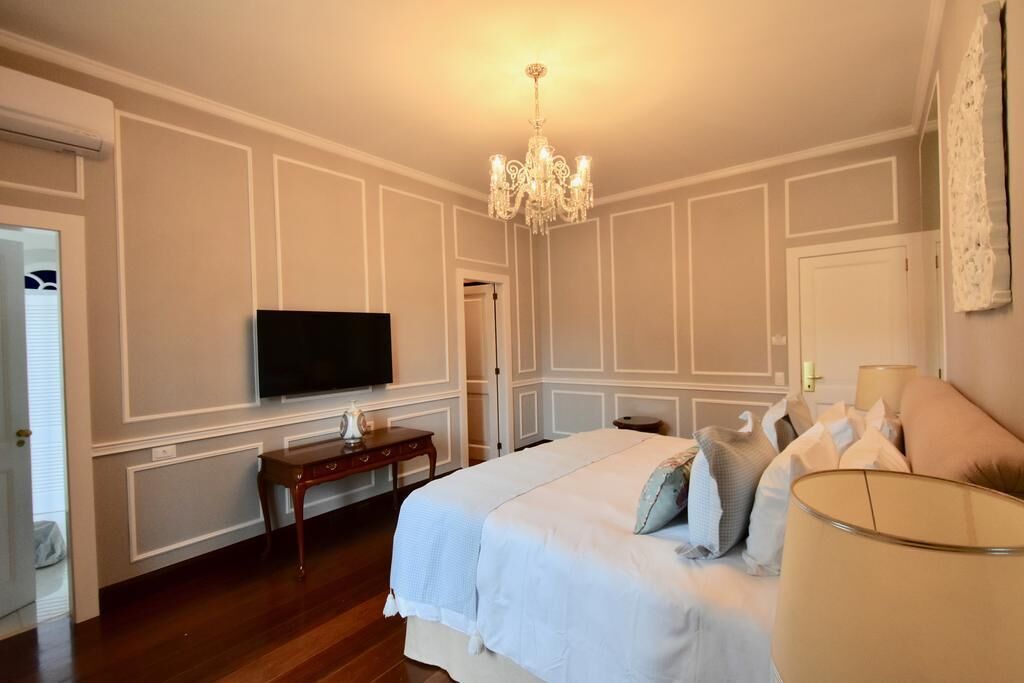 Un dormitorio con una cama grande, televisión, candelabro y mesita de noche.