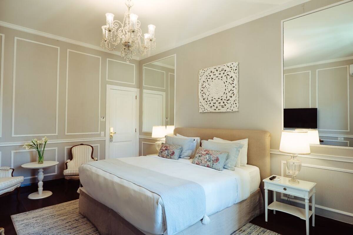 A bedroom with a large bed, a chandelier, a mirror, and a small table with a lamp.