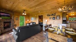 En mysig stuga med en öppen spis, en svart lädersoffa, ett matbord dukat med gula muggar och träpanel på väggarna.