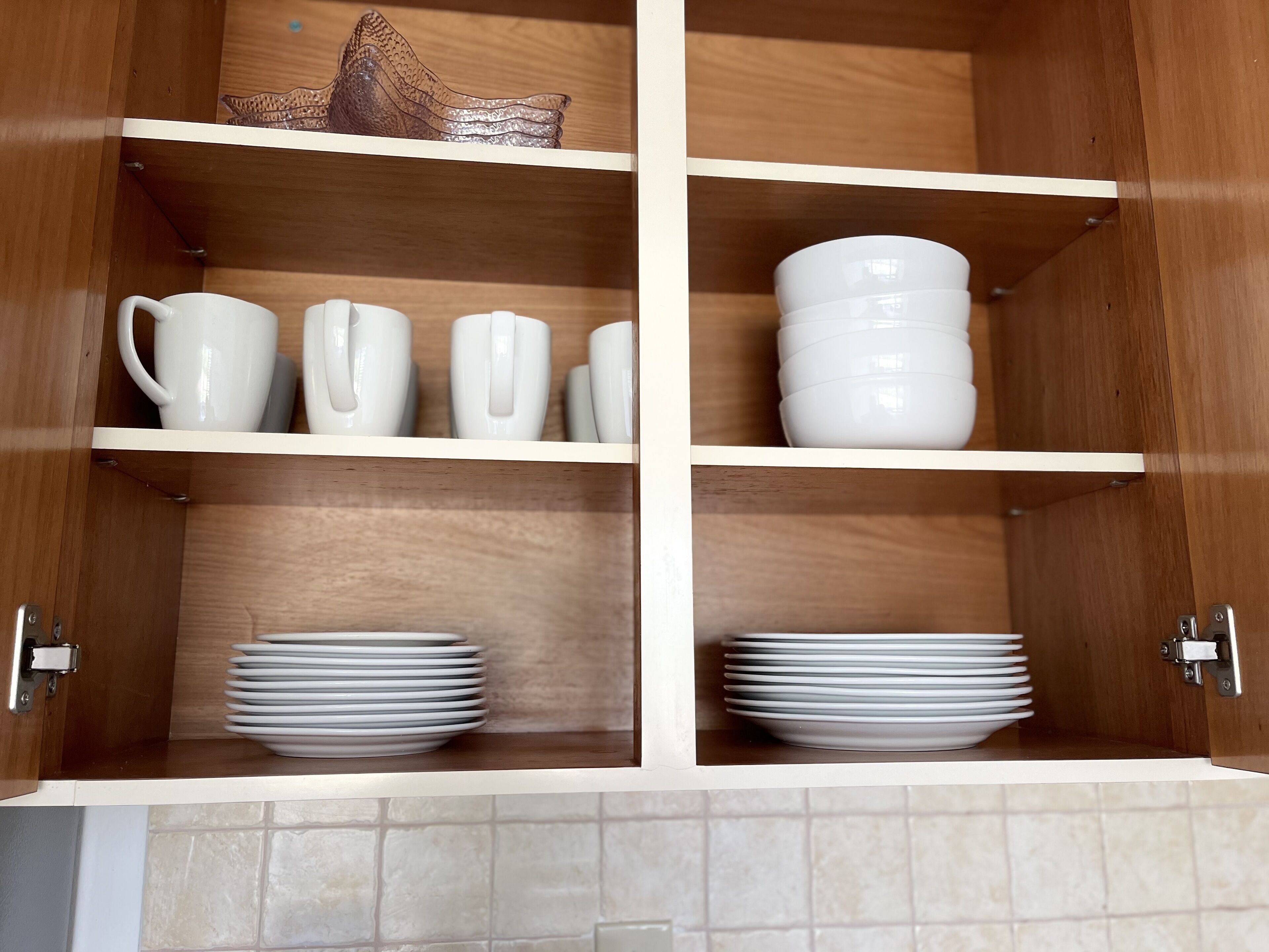 A wooden cabinet with shelves holding white mugs, cups, and plates.