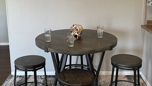 A dining area with a round table, two stools, and a wall-mounted clock. - Heart of the Loess Hills (Moorhead)