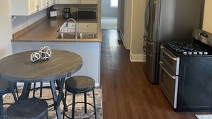 A modern kitchen with white cabinets, a stainless steel refrigerator, and a dining area with a round table and stools. - Heart of the Loess Hills (Moorhead)