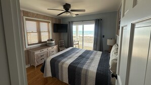 Ein Schlafzimmer mit einem Bett, einem Deckenventilator, einem Fernseher, einem Schreibtisch und Blick auf den Strand.