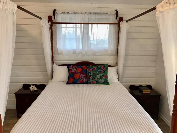 A four-poster canopy bed with white linens and colorful embroidered pillows.