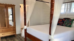 Un letto a baldacchino con biancheria bianca, un armadio in legno e una finestra con tende leggere.