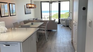 A modern kitchen with a Bosch dishwasher, a dining area with a white table and chairs, and a view of the ocean through large sliding glass doors.