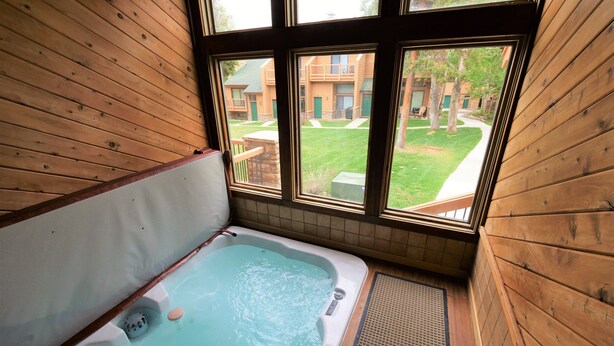 A wooden cabin with a hot tub and a view of a green lawn and buildings. - Beautiful Ski In/Out Cedars Townhome with Private Hot Tub (Breckenridge)