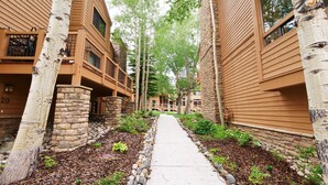 A pathway flanked by buildings with stone pillars and wooden siding, leading to a gated entrance. - Beautiful Ski In/Out Cedars Townhome with Private Hot Tub (Breckenridge)