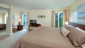Habitación de hotel con una cama grande, televisión, escritorio y vistas a árboles por la ventana.