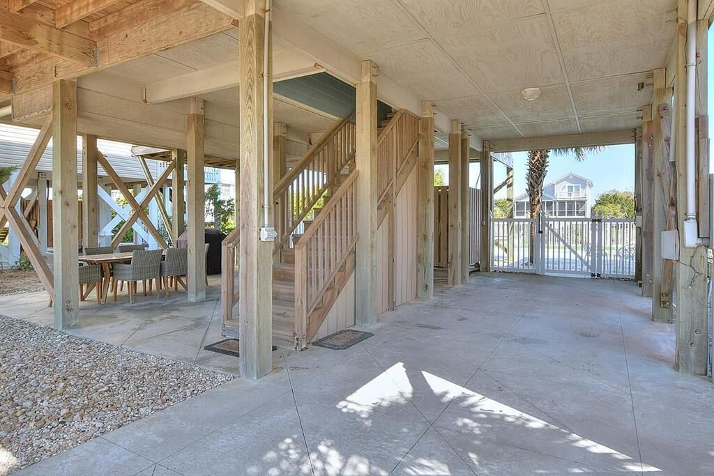 A covered outdoor area with a wooden staircase, a dining table with chairs, and a view of a residential area in the background.