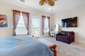A bedroom with a bed, a desk, a chair, a TV, and a balcony with curtains.