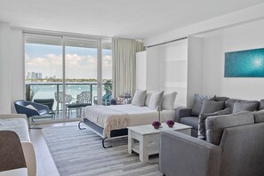 Enjoy a city and sea view from the large balcony, featuring a comfortable bed, sofa, and seating area.