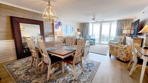 A spacious living room with a wooden dining table, comfortable seating, a large mirror, and a ceiling fan. - Hamilton 202, Oceanfront, Litchfield by the Sea (Pawleys Island)
