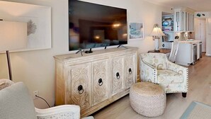 A living room with a large TV, a cabinet, a patterned armchair, and a small ottoman. - Hamilton 202, Oceanfront, Litchfield by the Sea (Pawleys Island)