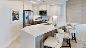 A modern kitchen with white cabinetry, stainless steel appliances, and a central island with bar stools. - Hamilton 202, Oceanfront, Litchfield by the Sea (Pawleys Island)