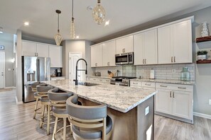 A modern kitchen with white cabinets, a granite countertop, a stainless steel refrigerator, and a gas stove.