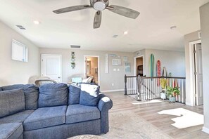 A spacious living room with a gray sofa, a ceiling fan, and a staircase leading to an upper level.