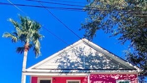 A two-story house with a pink exterior, a front porch, and a staircase leading to the second floor. - The Pink House- minutes walk to beach!! (Galveston)