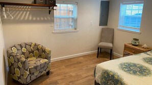 A bedroom with a bed, a chair, two windows, a shelf, and a small table. - The Pink House- minutes walk to beach!! (Galveston)