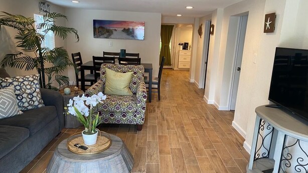 A living room with a sofa, a patterned armchair, a coffee table with a plant, and a television on a stand. - The Pink House- minutes walk to beach!! (Galveston)