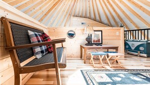 A cozy interior of a wooden yurt with a round ceiling, a sofa with plaid cushions, a small table with a lamp, and a vintage camper. - Comfy, Cozy, Luxury Yurt, Fun w/Private Hot Tub & Gas Grill, Large Deck (Pigeon Forge)