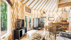 A wooden cabin interior with a TV, refrigerator, dining table, chairs, and a sofa. - Comfy, Cozy, Luxury Yurt, Fun w/Private Hot Tub & Gas Grill, Large Deck (Pigeon Forge)