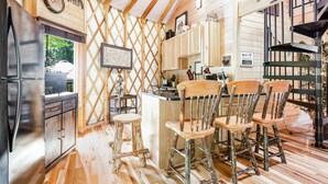 A rustic kitchen with wooden cabinets, a refrigerator, and a wooden dining area with chairs. - Comfy, Cozy, Luxury Yurt, Fun w/Private Hot Tub & Gas Grill, Large Deck (Pigeon Forge)
