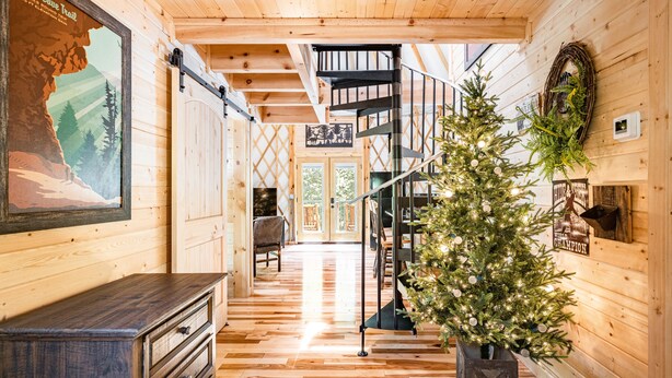 A wooden interior with a spiral staircase, a Christmas tree, and a framed poster on the wall. - Comfy, Cozy, Luxury Yurt, Fun w/Private Hot Tub & Gas Grill, Large Deck (Pigeon Forge)