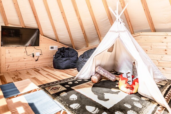 A cozy tented room with a television mounted on the wall, a patterned rug, and a sleeping bag. - Comfy, Cozy, Luxury Yurt, Fun w/Private Hot Tub & Gas Grill, Large Deck (Pigeon Forge)