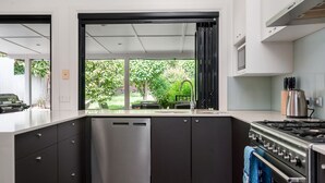 Une cuisine moderne équipée d’un lave-vaisselle intégré, d’une cuisinière à gaz et offrant une vue sur un jardin luxuriant grâce à une grande fenêtre.