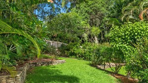 Un jardin luxuriant, avec une grande variété de plantes et d’arbres, un mur de soutènement en pierre et une pelouse bien entretenue.