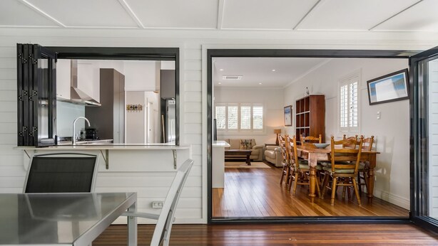 Une cuisine moderne avec un coin repas vitré, un plancher en bois et une vue sur un salon comprenant un canapé et une table à manger.