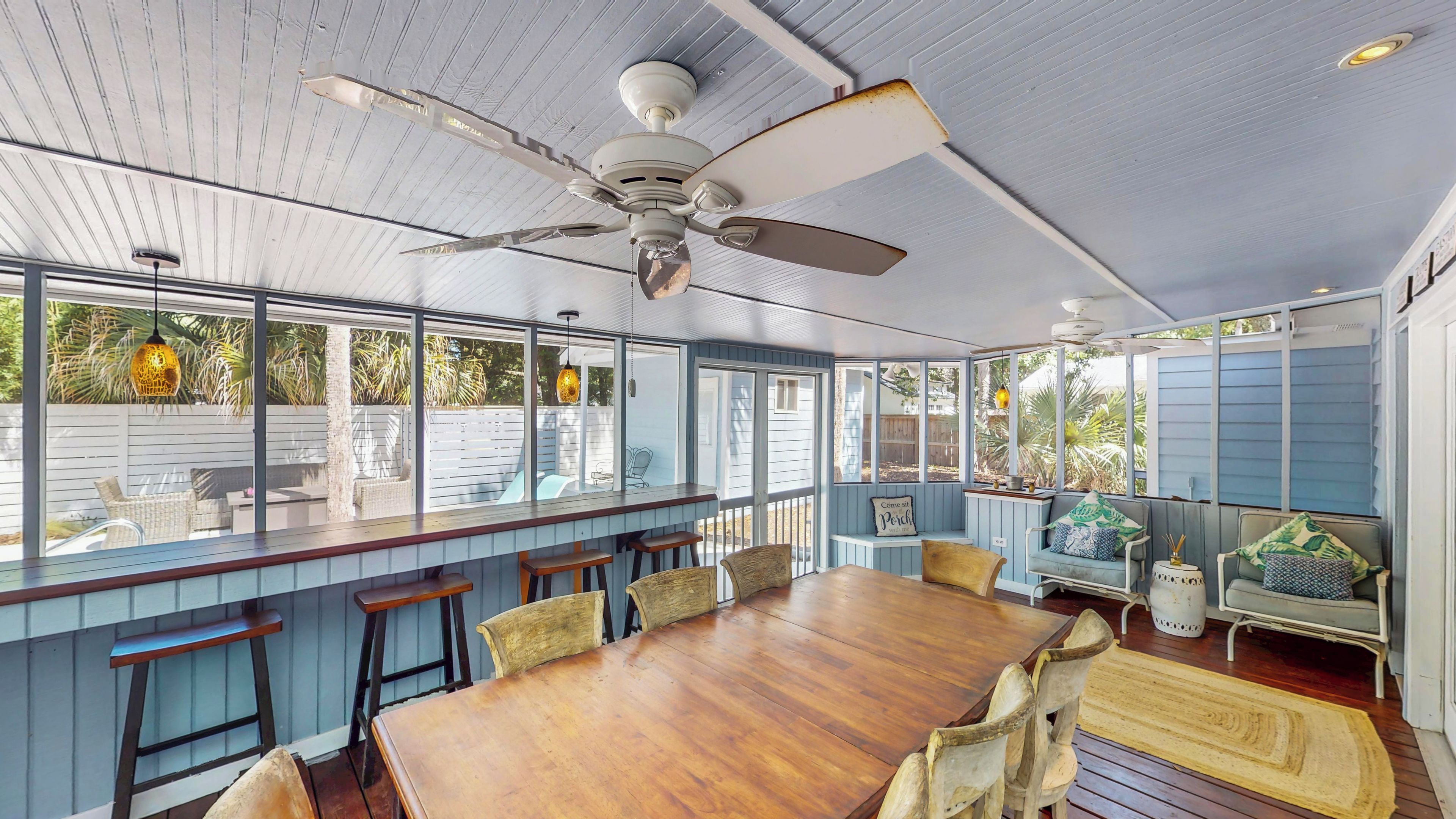 Un espace extérieur abrité, aménagé pour les repas, avec une table et des chaises en bois, un comptoir de bar et un ventilateur de plafond.