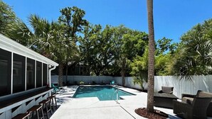 Un jardin avec une piscine, un espace salon extérieur et un coin abrité équipé de tabourets de bar.