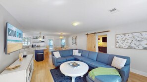 A modern living room with a sectional sofa, a round coffee table, and a kitchen in the background. - Daydream Oasis with private pool, screen porch with dining, sleeps 8! (Isle of Palms)