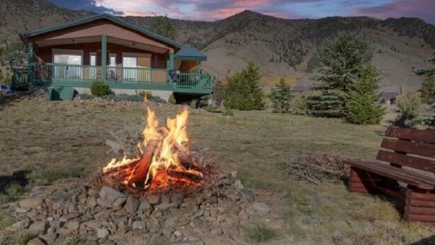 A lodge with a fire pit in front, surrounded by mountains.