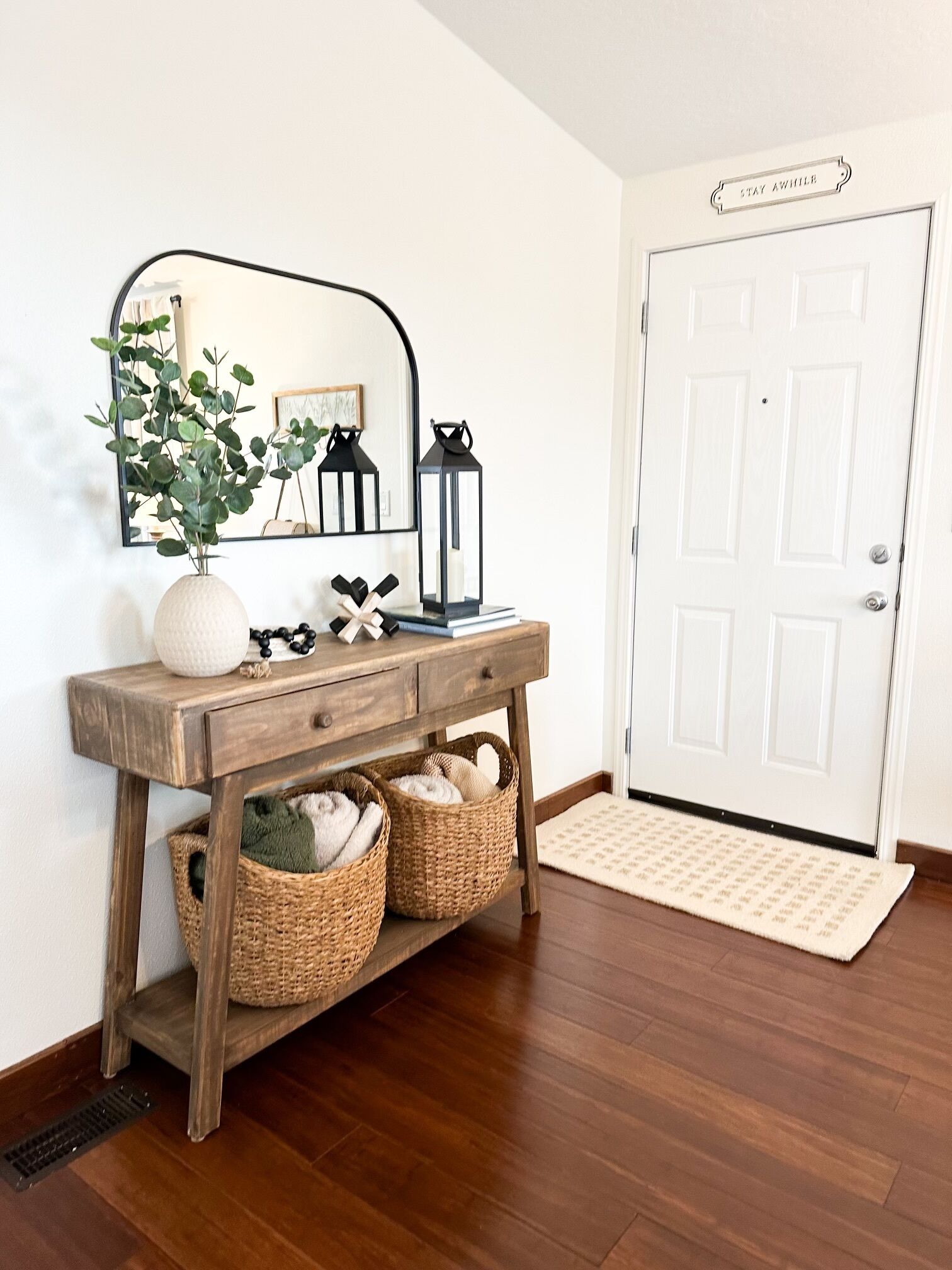 A wooden console table with baskets, a mirror, and decorative items.
