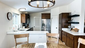 A modern kitchen with wooden cabinets, a stainless steel refrigerator, and a dining area with a round table and chairs.