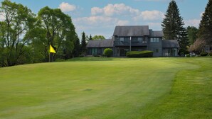 A golf course with a flag, a modern house with a balcony, and surrounding trees. - Balcony with Lake Michigan and golf view (Cedar)
