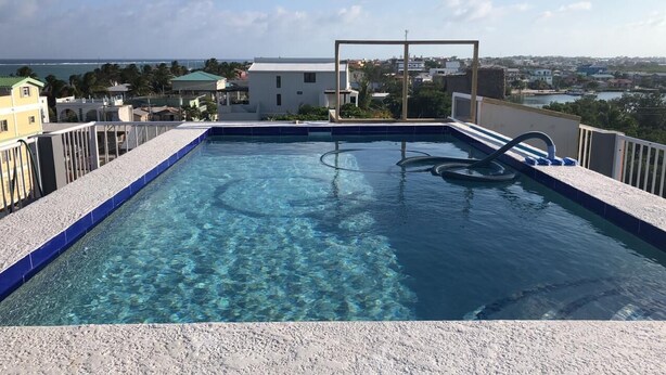 A rooftop infinity pool with clear water, surrounded by a white deck and a metal railing. - comfortable stay! perfect location amazing sun and reef view (BELIZE)