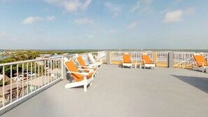 A rooftop terrace with white and orange lounge chairs, a white railing, and a view of the sea and buildings. - comfortable stay! perfect location amazing sun and reef view (BELIZE)