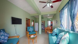 A living room with a sofa, armchair, and coffee table, a ceiling fan, and a television. - comfortable stay! perfect location amazing sun and reef view (BELIZE)