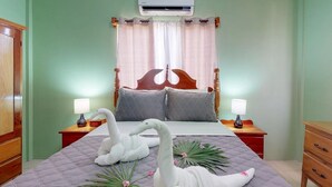 A bedroom with a bed, two bedside tables, a wooden wardrobe, and an air conditioning unit. - comfortable stay! perfect location amazing sun and reef view (BELIZE)